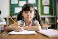 Portrait of little Asian girl writing or drawing in notebook at desk in classroom and looking at camera at the elementary school. Royalty Free Stock Photo