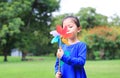 Portrait of little Asian kid girl blowing wind turbine in the summer garden Royalty Free Stock Photo