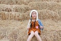 Portrait of little Asian kid girl in a hood on head and warm clothes sitting on pile of straw on a winter season Royalty Free Stock Photo