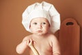 Portrait little baby boy in a chef`s hat sitting on the table holds a wooden rolling pin on a brown background. Copy, empty space Royalty Free Stock Photo