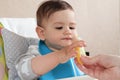 Portrait of little baby boy eating food. Baby with a spoon in feeding chair. Cute baby eating first meal