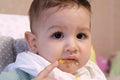 Portrait of little baby boy eating food. Baby with a spoon in feeding chair. Cute baby eating first meal