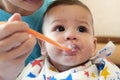 Portrait of little baby boy eating food. Baby with a spoon in feeding chair. Cute baby eating first meal