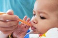 Portrait of little baby boy eating food. Baby with a spoon in feeding chair. Cute baby eating first meal