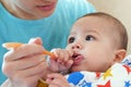 Portrait of little baby boy eating food. Baby with a spoon in feeding chair. Cute baby eating first meal