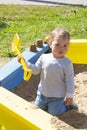 Portrait of a little baby boy girl playing in a sandbox with a yellow plastic shovel. Cute kid on a walk playing with sand, Royalty Free Stock Photo