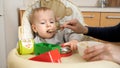 Portrait of little baby boy playing with toys while mother is feeding him in highchair. Concept of parenting, healthy nutrition Royalty Free Stock Photo