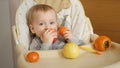 Portrait of little baby boy sitting in highchair and eating fruits at kitchen. Concept of parenting, healthy nutrition and baby Royalty Free Stock Photo