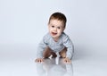 Portrait of little baby boy toddler in grey casual jumpsuit lying on floor, looking at camera and smiling over white background Royalty Free Stock Photo