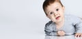 Portrait of little baby boy toddler in grey casual jumpsuit lying on floor and smiling over white wall background