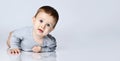 Portrait of little baby boy toddler in grey casual jumpsuit lying on floor and smiling over white wall background Royalty Free Stock Photo