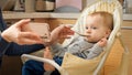 Portrait of little baby boy watching cartoons on smartphone while eating porridge in highchair. Concept of parenting, healthy Royalty Free Stock Photo