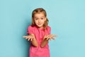 Portrait of little beautiful girl, child in pink T-shirt posing with questioning expression isolated over blue studio