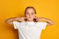 Portrait of little beautiful girl, child in white T-shirt posing, making funny faces isolated over yellow studio Royalty Free Stock Photo