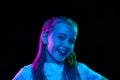 Portrait of little beautiful girl, child in white T-shirt posing, smiling isolated over black studio background in neon Royalty Free Stock Photo