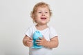 Portrait of little blond boy, dressed in white shirt, posing isolated over light background with blue bottle for baby food, wants Royalty Free Stock Photo