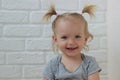 Portrait of little blond girl at the white brick wall,happy smiling toddler at home,sweet european child looking at