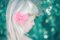 Portrait of little blonde Caucasian girl with pink hair bow. Pretty pensive sad child kid. Girly girl with red hair clip looking