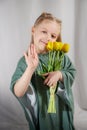 Portrait of a little blonde girl with a bouquet of spring yellow flowers on a light background. Child in green dress Royalty Free Stock Photo