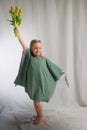 Portrait of a little blonde girl with a bouquet of spring yellow flowers on a light background. Child in green dress Royalty Free Stock Photo