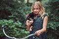 Portrait of a little blonde girl in a casual dress, holds cute spitz dog, in a park.