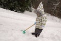 Portrait of little boy in bright winter clothes with shovel standing in snow. Background of winter park Royalty Free Stock Photo