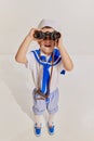 Portrait of little boy, child in image of seaman in vest posing with binoculars over grey background. Amazed traveler Royalty Free Stock Photo