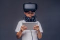 Portrait of a little boy dressed in a white t-shirt, with virtual reality glasses and headphones and using a digital Royalty Free Stock Photo