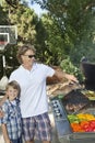 Portrait of a little boy with father barbecuing vegetable on barbecue grill in lawn Royalty Free Stock Photo