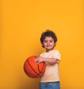 Portrait of a little boy holding a basket ball isolated on yellow. Kid in sport wear. Small child smiling. Sport child Royalty Free Stock Photo