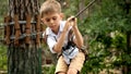 Portrait of little boy holding tight safety cable while walking on rope bridge at extreme adventure park. Kids sports, summer Royalty Free Stock Photo