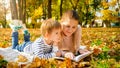 Portrait of little boy lying with his mother at autumn park and reading a book Royalty Free Stock Photo