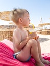 Portrait of little boy sitting on the sea beach and drinking orange juice from straw. Children relaxing and having good Royalty Free Stock Photo