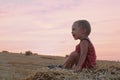 Portrait of little boy in a summer hat sitting on a haystack in a field of wheat