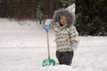 Portrait of little boy with thoughtful look in winter clothes with shovel standing in snow. Background of winter park Royalty Free Stock Photo