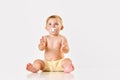 Portrait of little calm baby, toddler sitting with pacifier, clapping hands and looking against white studio background