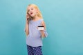 Portrait of little caucasian girl in blue t-shirt with long blonde hair holds a credit card isolated on blue background Royalty Free Stock Photo