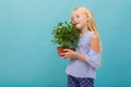 Portrait of little caucasian girl in blue t-shirt with long blonde hair holds a green plant isolated on blue background Royalty Free Stock Photo