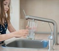 Portrait of a little caucasian girl gaining a glass of tap clean water. Kitchen faucet. Cute curly kid pouring fresh water Royalty Free Stock Photo