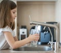 Portrait of a little caucasian girl gaining a glass of tap clean water. Kitchen faucet. Cute curly kid. Healthy life concept