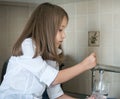 Portrait of a little caucasian girl gaining a glass of tap clean water. Kitchen faucet. Cute curly kid pouring fresh water from Royalty Free Stock Photo