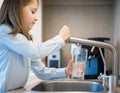 Portrait of a little caucasian girl gaining a glass of tap clean water. Kitchen faucet. Cute curly kid pouring fresh water from Royalty Free Stock Photo