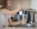 Portrait of a little caucasian girl gaining a glass of tap clean water. Kitchen faucet. Cute curly kid. Healthy life concept