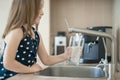 Portrait of a little caucasian girl gaining a glass of tap clean water. Kitchen faucet. Cute curly kid pouring fresh water Royalty Free Stock Photo