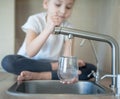 Portrait of little caucasian girl gaining a glass of tap clean water. Kitchen faucet. Kid pouring fresh water from filter tap. Royalty Free Stock Photo