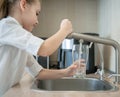 Portrait of little caucasian girl gaining a glass of tap clean water. Kitchen faucet. Kid pouring fresh water from filter tap. Royalty Free Stock Photo