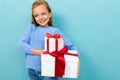 Portrait of little caucasian girl with long brow hair in blue hoody holds a white boxes with gifts isolated on blue Royalty Free Stock Photo