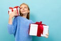 Portrait of little caucasian girl with long brow hair in blue hoody holds a white boxes with gifts isolated on blue Royalty Free Stock Photo