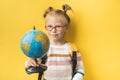 Portrait of little caucasian girl on the yellow background. Elementary school student wearing glasses and holding the globe Royalty Free Stock Photo