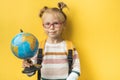 Portrait of little caucasian girl on the yellow background. Elementary school student wearing glasses and holding the globe Royalty Free Stock Photo